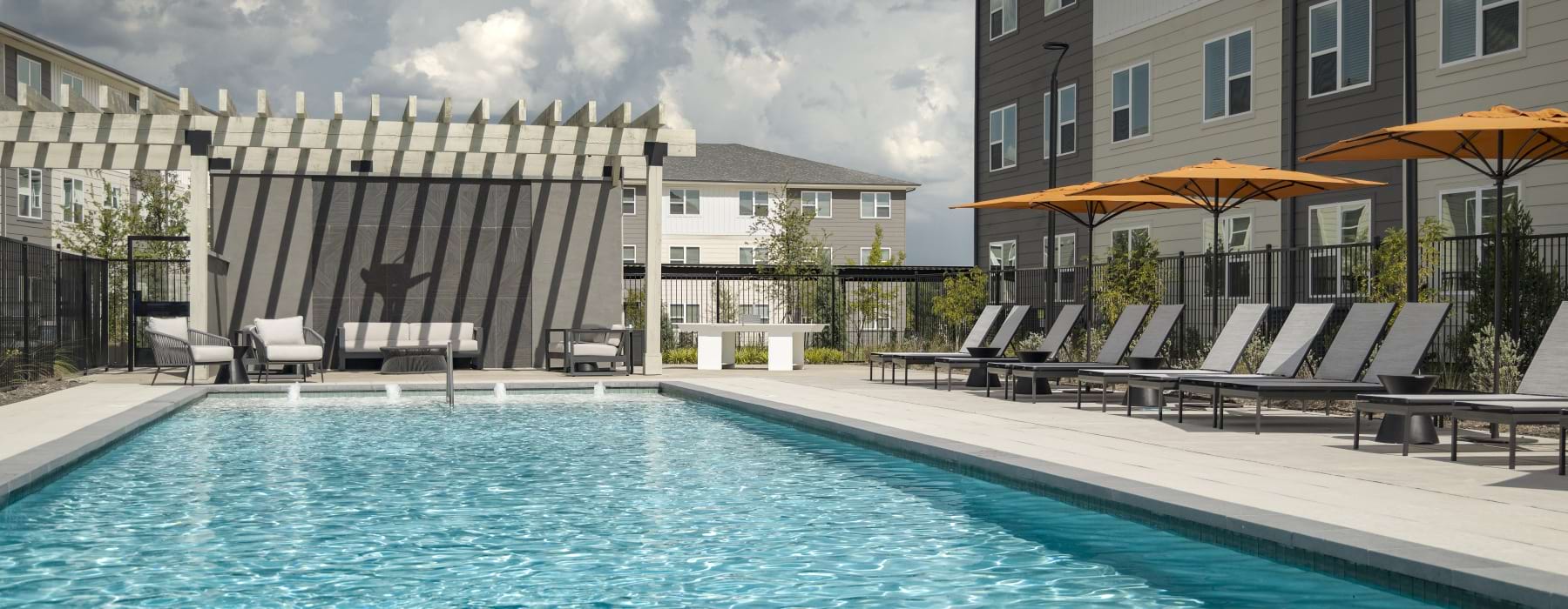 a crystal clear pool with lounge chairs and seating with an apartment on the side