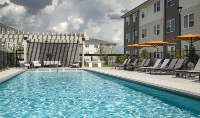 a crystal clear pool with lounge chairs and seating with an apartment on the side